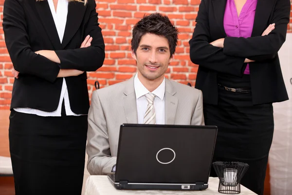 Leende affärsman med laptop omgiven av kvinnliga medarbetare — Stockfoto