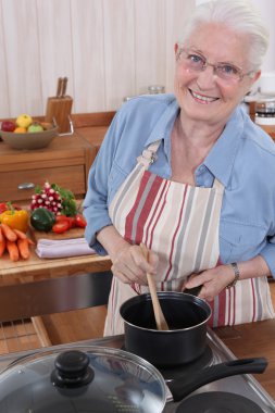 Elderly woman cooking in her kitchen clipart