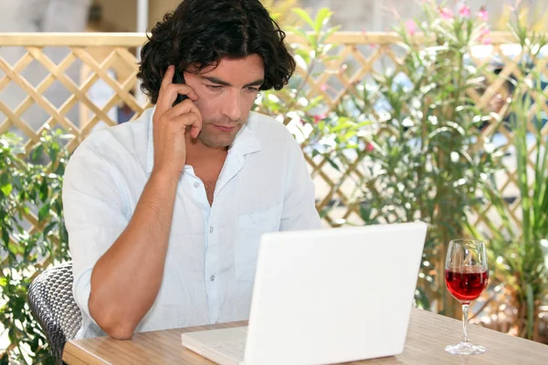 Man speaking on his mobile phone while drinking wine and surfing the Net on — Stock Photo, Image