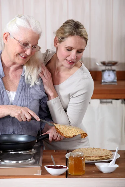 A mature mother and her adult daughter making crepes. — Stock Photo, Image