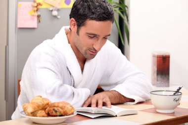 Handsome man reading a book at breakfast clipart