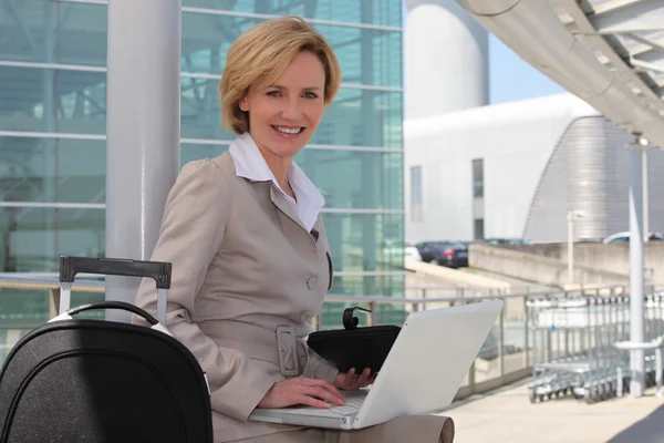 Empresária sorrindo no laptop fora do aeroporto — Fotografia de Stock