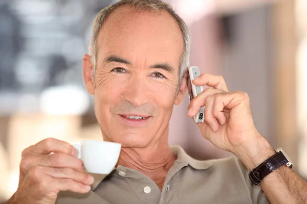 Γκρίζα μαλλιά άνθρωπος πίνει καφέ και μιλώντας σε κινητό τηλέφωνο — Φωτογραφία Αρχείου