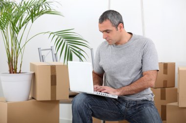 Man amid removal boxes working on laptop clipart