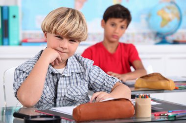 Schoolboys seated at desk in classroom clipart