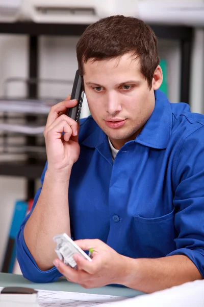 Eletricista verificando uma peça pelo telefone — Fotografia de Stock
