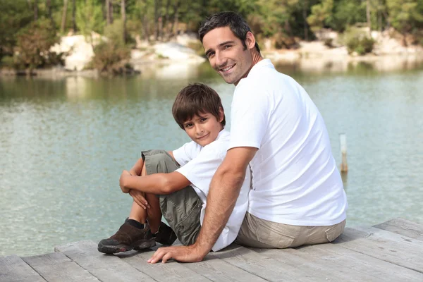 Ein Vater und sein Sohn sitzen auf einem Ponton und blicken auf einen See — Stockfoto