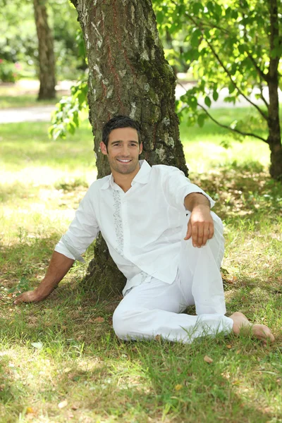 Человек в белом сидит под деревом — стоковое фото