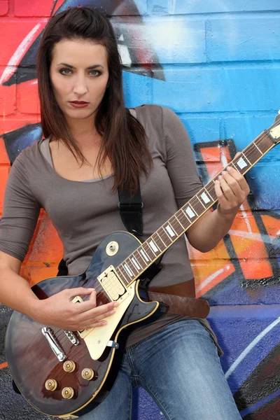 Etiketli bir duvarın önünde kadın gitarist — Stok fotoğraf