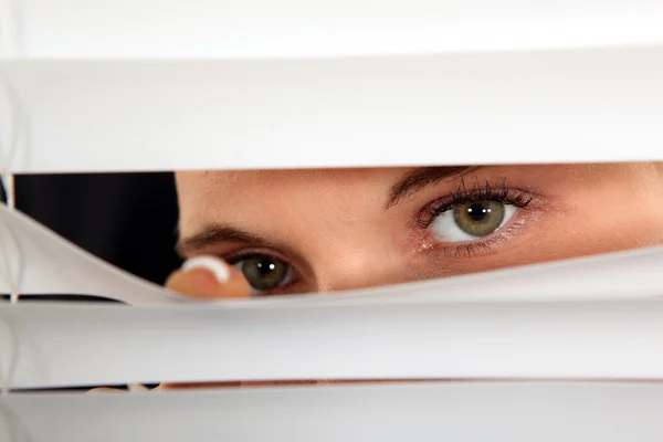 Nahaufnahme der Augen einer Frau, die durch Jalousien spioniert — Stockfoto