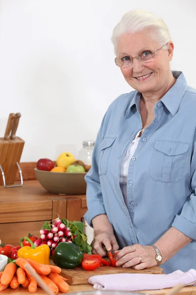 Mulher idosa cortando legumes — Fotografia de Stock