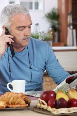 Mature man having breakfast and reading newspaper clipart