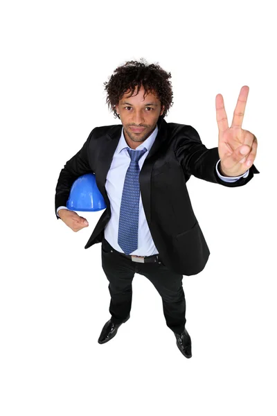 Un hombre con un traje sosteniendo un casco y dando la señal de paz —  Fotos de Stock