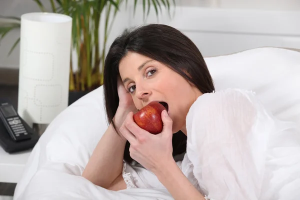 Mulher comendo maçã na cama — Fotografia de Stock