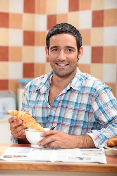 Homem enterrando um croissant em um café com leite na hora do almoço — Fotografia de Stock