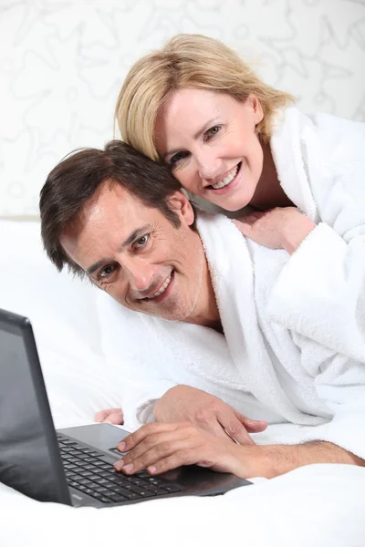 드레싱 가운에 휴대용 퍼스널 컴퓨터에 행복 한 커플. — 스톡 사진