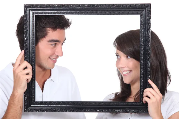Young couple behind photo frame — Stock Photo, Image