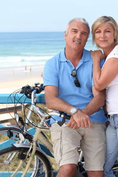 Una pareja de mediana edad en bicicleta junto a la orilla del mar . — Foto de Stock
