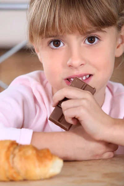 Little girl eating chocolate bar for breakfast — Stock Photo, Image