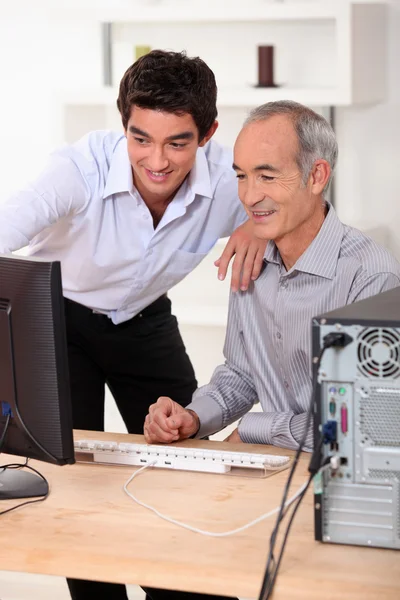 Homens mais jovens e mais velhos olhando para um computador — Fotografia de Stock