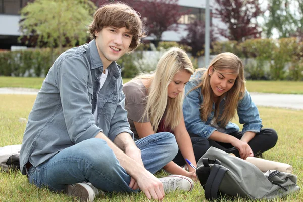 Três estudantes sentados na grama de um campus . — Fotografia de Stock