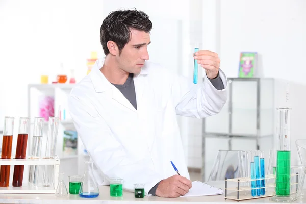 Young man studying the contents of a test tube and making notes accordingly — Stock Photo, Image