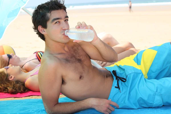 Mladý člověk pije na pláži — Stock fotografie