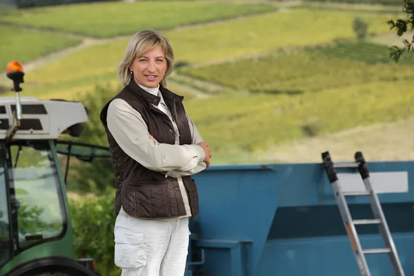 45 år gammal kvinna framför en traktor och vinstockar — Stockfoto