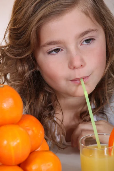 Little girl drinking orange juice through straw — Stock Photo, Image