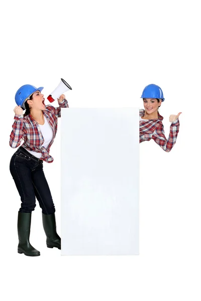 Craftswoman shouting in loudspeaker and twin sister — Stock Photo, Image
