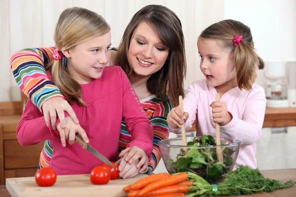 Mother chopping vegetables with two daughters — Stock Photo, Image