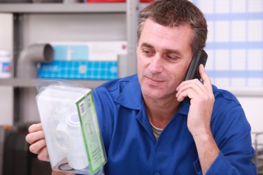 Plumbers merchant on the phone with a part in hand clipart