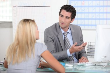 Suited man talking to a young woman across a desk clipart