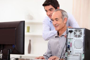 Young man teaching an elderly man computer skills clipart