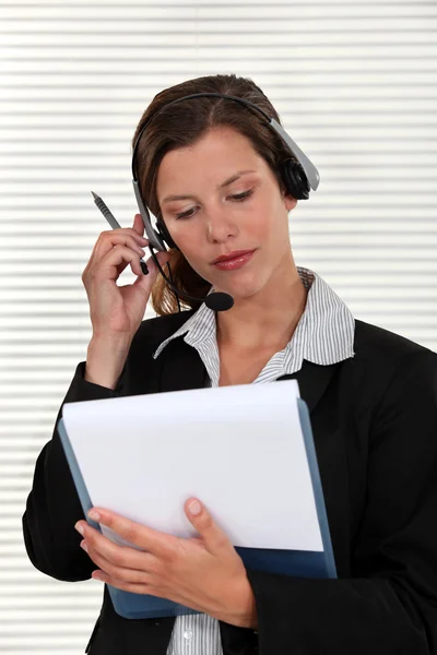 Woman adjusting her headset and holding a clipboard — Stock Photo, Image