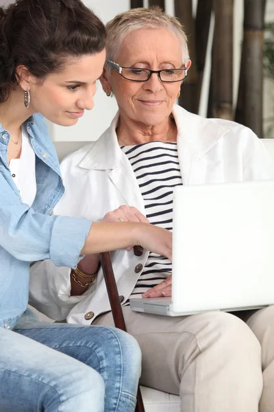 Ung kvinna att hjälpa en äldre dam navigera på internet — Stockfoto