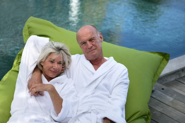 Bejaarde echtpaar liggend op opblaasbare matras op een pool dek — Stockfoto