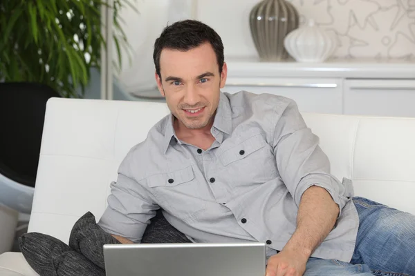 Man with laptop lying on a couch — Stock Photo, Image