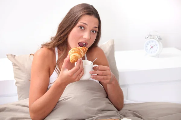 Mulher comendo um croissant na cama — Fotografia de Stock