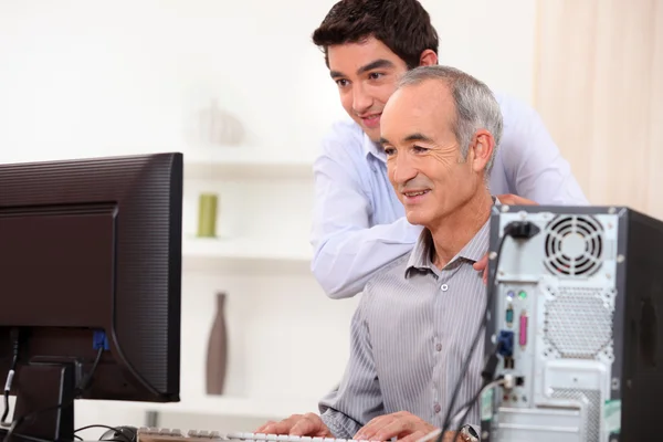Молодой человек обучает пожилого человека навыкам работы с компьютером — стоковое фото