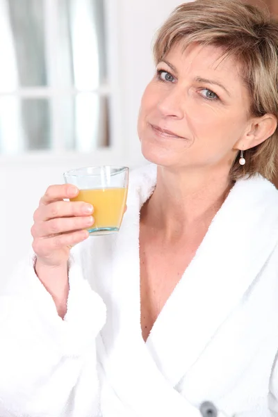 Женщина в халате пьет апельсиновый сок — стоковое фото