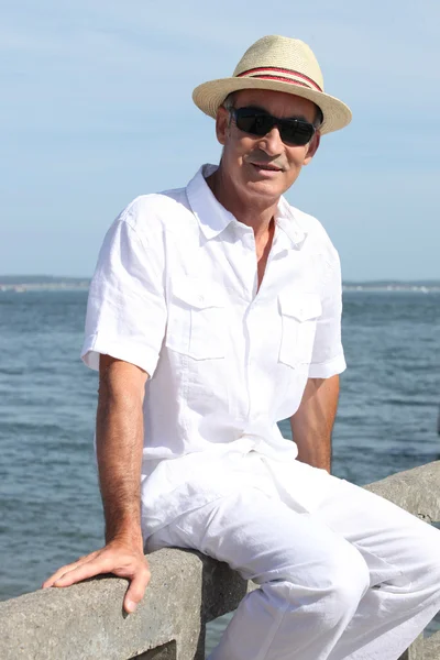 Deniz kenarında bir duvarda oturan yaşlı adam — Stok fotoğraf