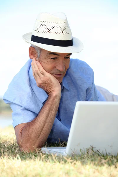 Пожилой человек лежит в поле с ноутбуком — стоковое фото