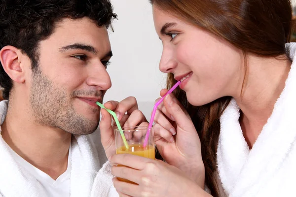 Paar trinkt Orangensaft aus demselben Glas mit Strohhalmen — Stockfoto