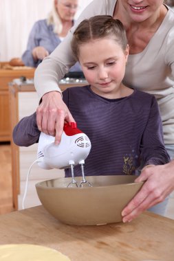 Woman helping her daughter use a hand mixer clipart