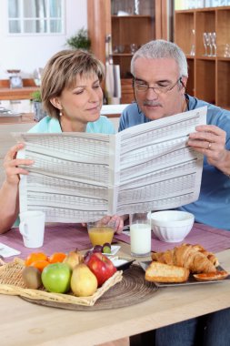 Couple reading the newspaper over breakfast clipart