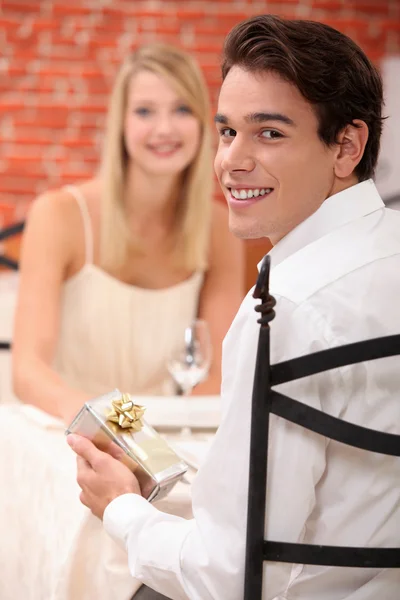 Młody człowiek, dając prezent do swojej dziewczyny w restauracji — Zdjęcie stockowe
