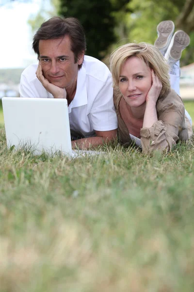 Пара лежащих в траве с помощью ноутбука — стоковое фото