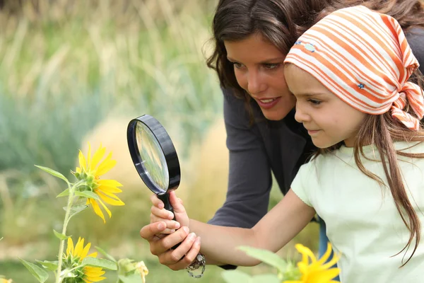 母と娘の虫眼鏡で花を見ています。 — ストック写真