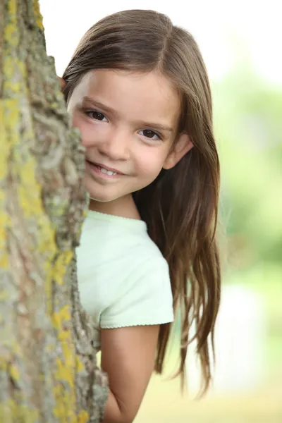 Młoda dziewczyna, chowając się za drzewa — Zdjęcie stockowe
